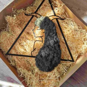 Zapakowana dekoracja z chrobotka reniferowego w kształcie trójkąta, przedstawiająca znak zodiaku Koziorożec, umieszczona w ekologicznym kartonowym pudełku z zabezpieczeniem do transportu; rękodzieło gotowe do wysyłki, prezentowe opakowanie podkreślające naturalny i ekologiczny charakter produktu.