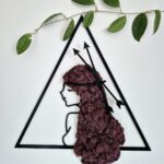 Ręcznie wykonany obraz z chrobotka reniferowego w intensywnym odcieniu fioletu, przedstawiający kobiecą postać symbolizującą znak zodiaku Strzelec. Kobieta ma bujne włosy z fioletowego chrobotka, w których znajdują się symboliczne strzały.