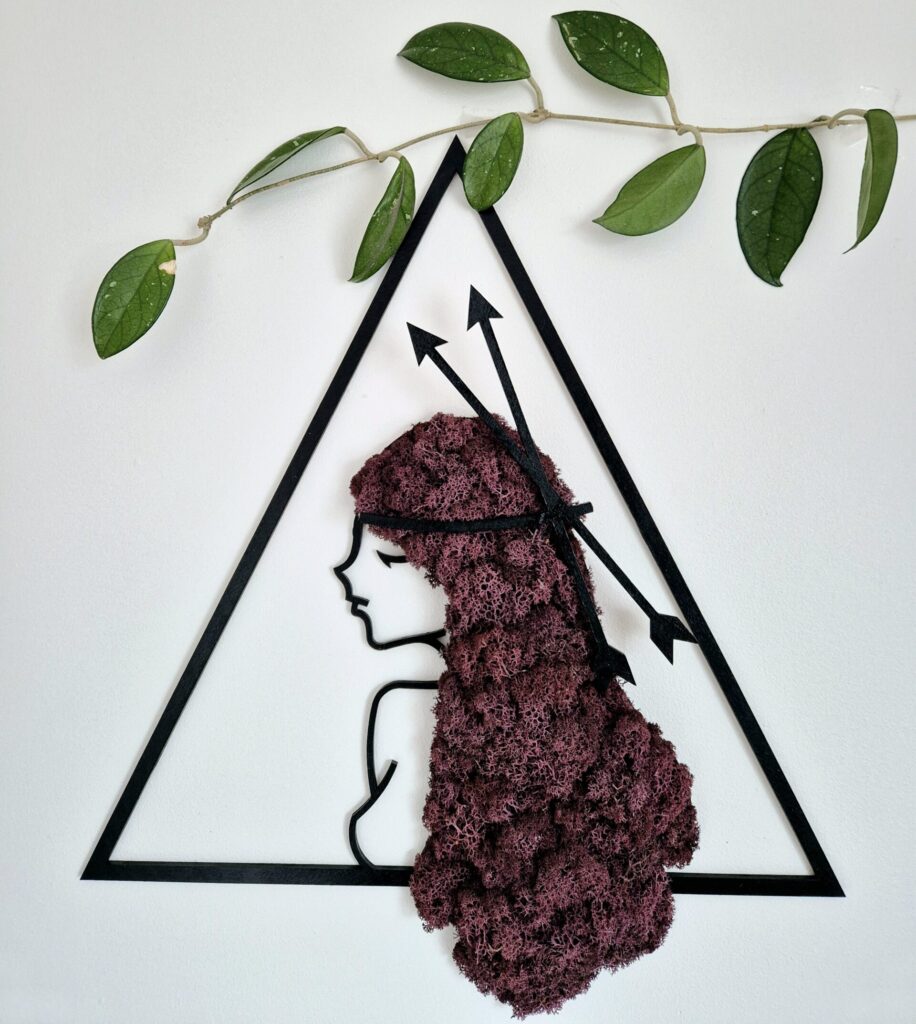 Ręcznie wykonany obraz z chrobotka reniferowego w intensywnym odcieniu fioletu, przedstawiający kobiecą postać symbolizującą znak zodiaku Strzelec. Kobieta ma bujne włosy z fioletowego chrobotka, w których znajdują się symboliczne strzały.