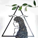 Obraz dekoracyjny z naturalnego szarego chrobotka reniferowego przedstawiający kobiecą postać znaku zodiaku Koziorożec z rogami na głowie, w czarnej trójkątnej ramie o wymiarach 45 cm; rękodzieło w stylu boho i japandi, nasycone energią Reiki, symbolizujące siłę, wytrwałość i duchową harmonię.