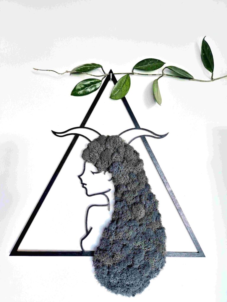 Obraz dekoracyjny z naturalnego szarego chrobotka reniferowego przedstawiający kobiecą postać znaku zodiaku Koziorożec z rogami na głowie, w czarnej trójkątnej ramie o wymiarach 45 cm; rękodzieło w stylu boho i japandi, nasycone energią Reiki, symbolizujące siłę, wytrwałość i duchową harmonię.